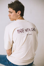 Load image into Gallery viewer, Male model sitting on chair styling the cream conscious collection t-shirt