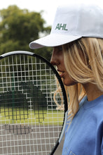 Load image into Gallery viewer, Female leaning tennis racket on face while modelling white AHL cap
