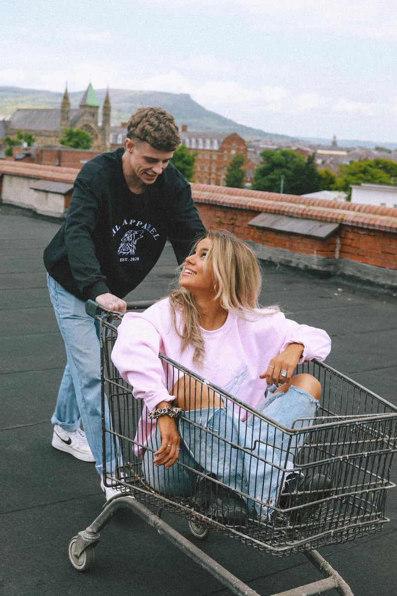 Female wearing pink sweatshirt in a trolley and male model wearing a green sweatshirt pushing her