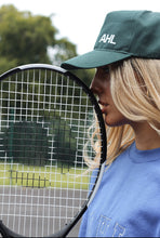 Load image into Gallery viewer, Female leaning tennis racket against face whilst wearing a khaki AHL cap
