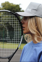 Load image into Gallery viewer, Female leaning tennis racket against her face whilst modelling grey AHL cap
