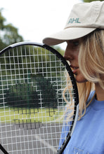 Load image into Gallery viewer, Female leaning tennis racket on face whilst modelling cream AHL cap
