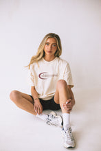 Load image into Gallery viewer, Female model sitting on floor styling cream conscious collection t-shirt
