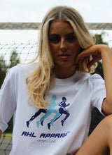 Load image into Gallery viewer, Female sitting on tennis court whilst modelling white Sports Luxe t-shirt
