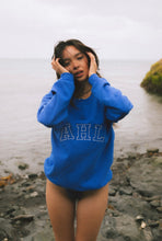 Load image into Gallery viewer, Female modelling blue signature sweatshirt on a beach
