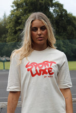 Load image into Gallery viewer, Female standing on tennis court modelling cream Sport Luxe t-shirt
