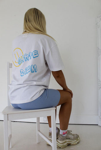 Female sitting on white chair showing the back of white carpe diem t-shirt