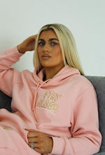 Load image into Gallery viewer, Female sitting on sofa modelling pink stay golden hoodie
