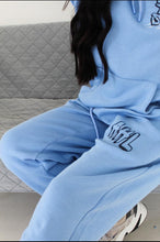 Load image into Gallery viewer, Female sitting on sofa modelling blue see you soon tracksuit
