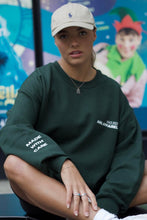 Load image into Gallery viewer, Female sitting on floor whilst modelling green MWC sweatshirt
