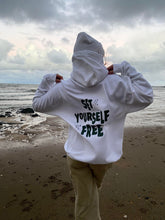 Load image into Gallery viewer, female modelling set yourself free hoodie and beanie in white on a beach
