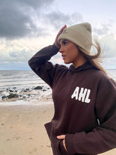 Load image into Gallery viewer, Female modelling brown hoodie and cream beanie on a beach
