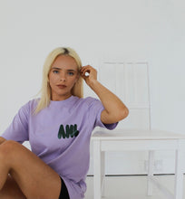 Load image into Gallery viewer, Model sitting on floor leaning against white chair to wear purple t-shirt
