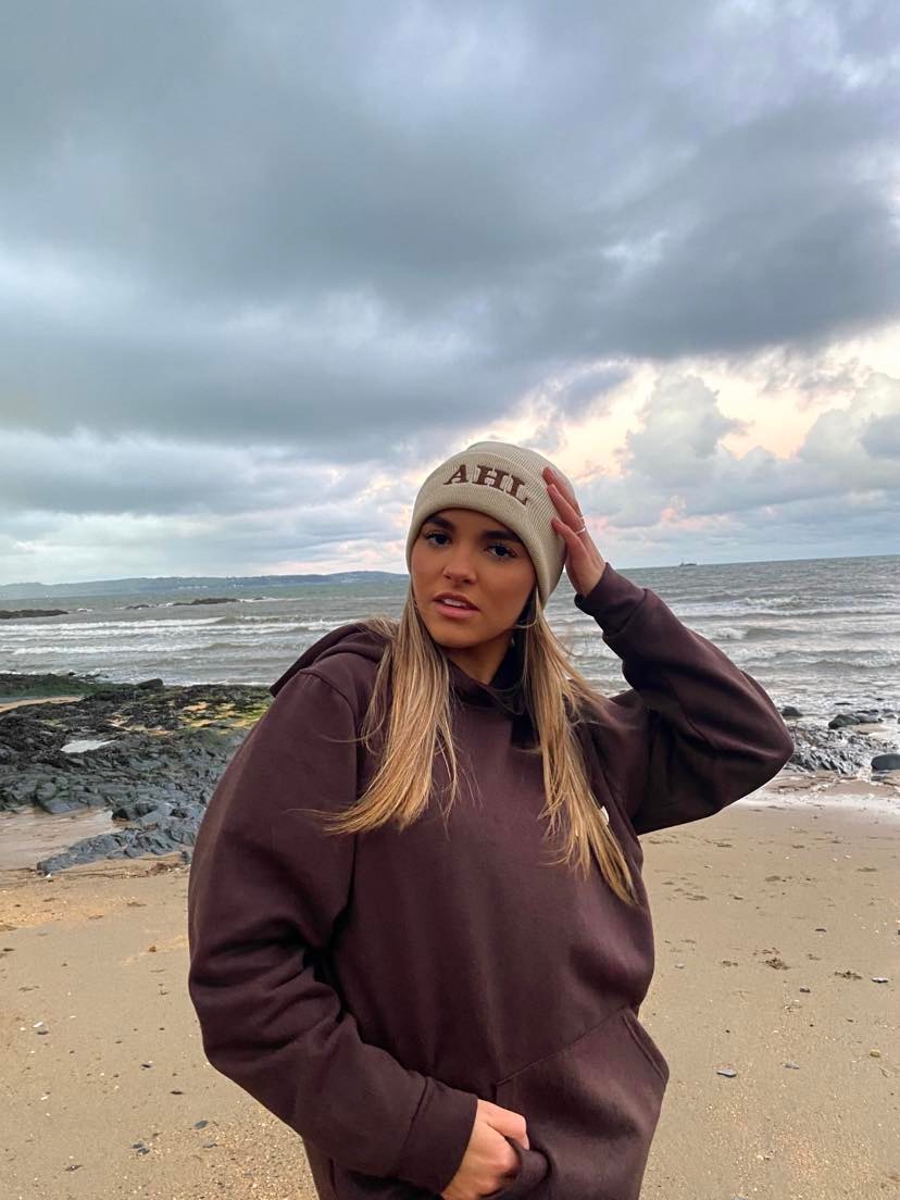 Female modelling brown hoodie and cream beanie on a beach