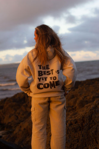 Female modelling the best is yet to come hoodie in cream on a beach