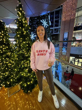 Load image into Gallery viewer, Female standing in front of Christmas trees modelling pink Santa baby sweatshirt
